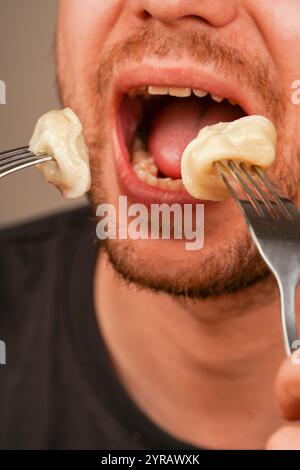 Ein fokussiertes Bild von Knödeln auf einer Gabel, die von einer Person genossen werden, symbolisiert das Vergnügen, frisch zubereitete Komfortgerichte zu essen. Ein Mann isst Stockfoto