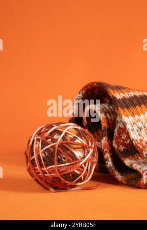 Eine Kugel aus mehrfarbigem Wollgarn in Nahaufnahme auf orangem Hintergrund. Materialien für handgefertigte Strickwaren Stockfoto