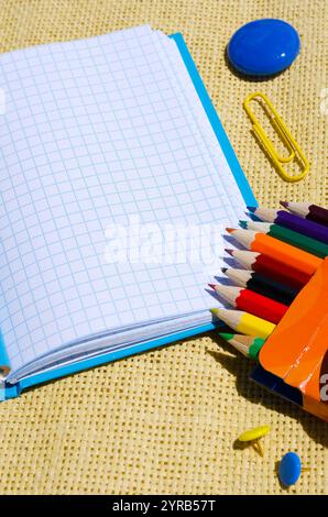 Schulkonzept auf Sackleinen-Hintergrund. Notizblock, Bleistifte, Büroklammern, Knöpfe und Magnet. Stockfoto