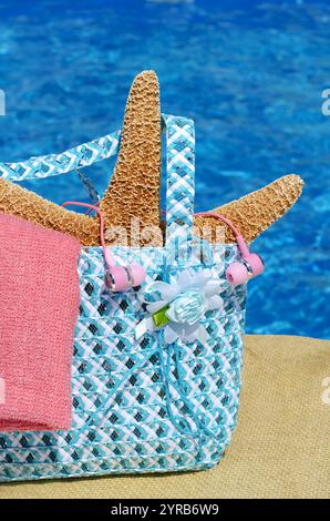 Seesterne und Kopfhörer in einer Damentasche vor dem Hintergrund des Poolkonzepts der Entspannung. Sommerurlaub mit der Familie Stockfoto