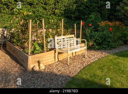 Eine alte und verwitterte Gartenbank neben einem Hochbeet mit Himbeeren und Rhabarden in einem Devon Garten Stockfoto