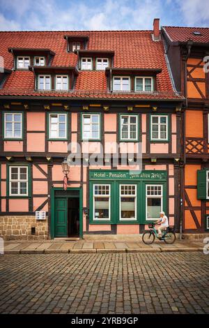 Ein charmantes historisches Gebäude in Quedlinburg, Deutschland, mit einer Mischung aus rosa und Fachwerkarchitektur, mit einem Radfahrer, der auf einem Kopfsteinpflaster vorbeifährt Stockfoto