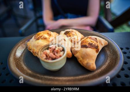 Ein Teller mit goldenen, knusprigen Knödeln oder Pierogi, serviert mit einer reichhaltigen roten Sauce, auf einem strukturierten schwarzen Tisch in Torun. Stockfoto