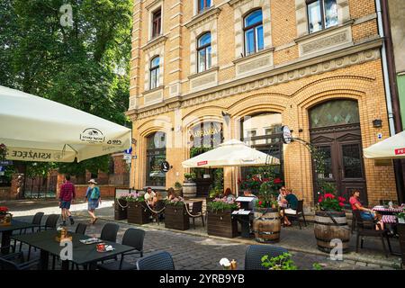 Ein lebhaftes Café im Freien in Torun mit einem historischen Backsteingebäude, Gästen, die ihre Mahlzeiten genießen, und farbenfrohen Blumenarrangements. Stockfoto