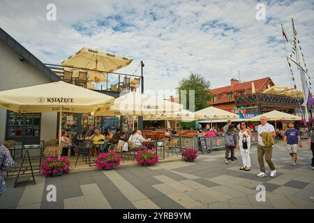 Ein lebhaftes Café im Freien in Polen, in dem Gäste ihre Mahlzeiten unter großen Sonnenschirmen genießen, umgeben von farbenfrohen Blumenarrangements und einem Stockfoto