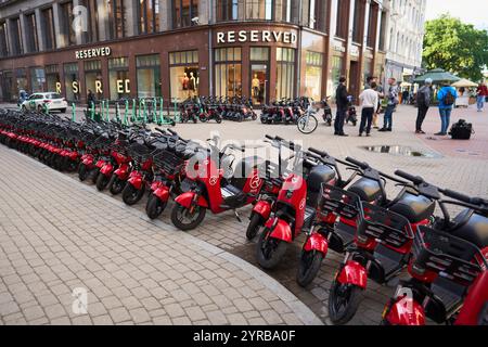 Eine lebhafte Szene in Riga, Lettland, mit Reihen roter Elektroroller, die auf einer kopfsteingepflasterten Straße geparkt sind, mit einem Bekleidungsgeschäft namens „Reserved“ im Stockfoto