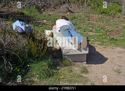 Der junge Mann liegt auf einer Steinbank in einem Park Stockfoto