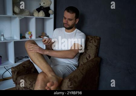 Der 30-jährige Mann trägt Feuchtigkeitscreme auf die Haut seiner Beine auf Stockfoto