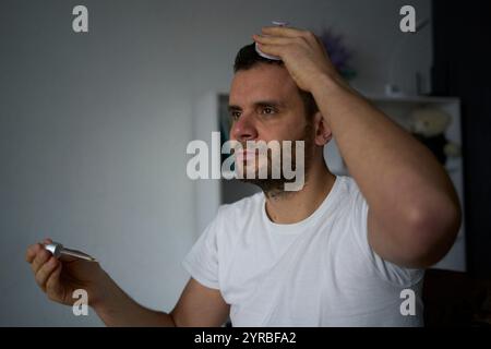 Ein 30-jähriger Mann wendet ein Produkt für Haarwuchs an, Behandlung von Kahlheit Stockfoto