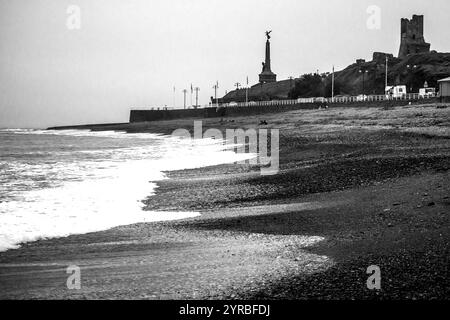 Schwarze und witzige Küste in Aberystwyth mit den Ruinen der mittelalterlichen Burg und dem Denkmal für den Weltkrieg im Hintergrund. Stockfoto