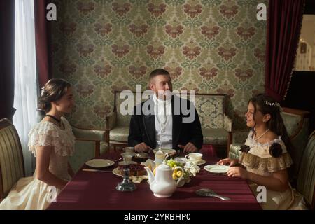 Gruppenszene am Esstisch mit drei elegant gekleideten Figuren, die sich im klassischen Interieur unterhalten Stockfoto