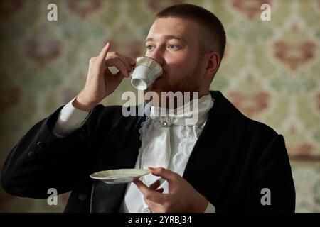 Seitenansicht Porträt eines klassischen jungen Gentlemans, der anmutig Tee trinkt und eine kleine Porzellanschale hält, Kopierraum Stockfoto