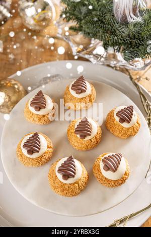 Weihnachtscremepuffs, dekoriert mit Schokoladenbäumen auf Marmorkuchenständer Stockfoto