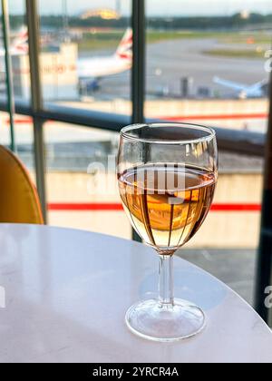 London, England, Großbritannien - 21. August 2024: Glas Rosenwein auf einem Tisch in einer Business-Lounge mit Blick auf die Flugzeuge von Bbritish Airways vor dem Terminal 5 Bu Stockfoto