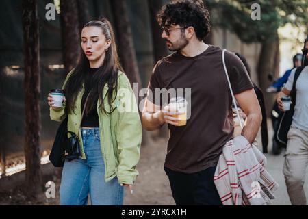 Eine junge Frau und ein Mann genießen einen entspannten Spaziergang mit Kaffee auf einem baumgesäumten Weg. Stockfoto