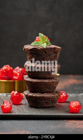 Schokoladen-Brownies, die perfekt gestapelt sind, mit saftigen Kirsch- und Minzblättern auf der Oberseite Stockfoto