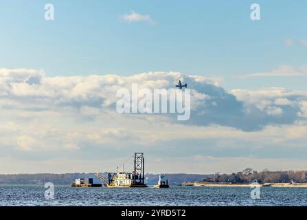 Ein tief fliegendes Militärflugzeug, das über ein Schlepper und Barke vor der Schutzinsel ny fliegt Stockfoto