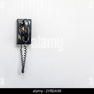 Altes schwarzes Drehtelefon an einer weißen Innenwand Stockfoto