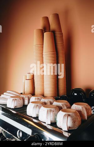 Gestapelte Pappbecher säumen die Oberseite der Kaffeemaschine, deren umweltfreundliches Design Stil und Nachhaltigkeit perfekt verbindet. Stockfoto
