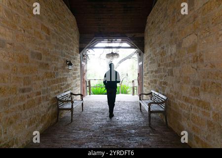 Silhouette eines Mannes, der durch einen rustikalen Steintunnel mit Bänken läuft Stockfoto