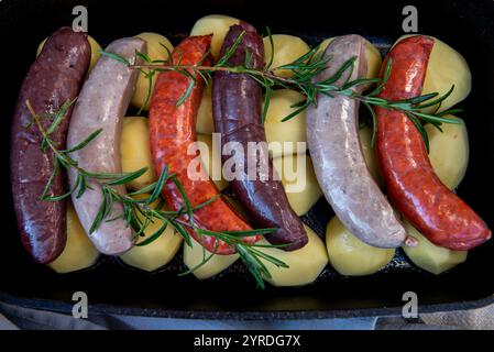 Rohe Würstchen im Ofen. Nahaufnahme einer Schüssel mit roher hausgemachter Blutwurst, Schweinefleisch und Chorizo im Ofen mit Kartoffeln. Hausgemachte traditionelle Speisen. Stockfoto