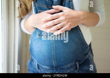 Nahaufnahme der Hände am Bauch der schwangeren Frau in Denim Overalls Stockfoto