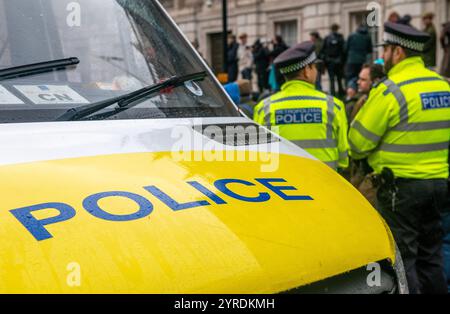 London, Großbritannien. November 2024. Zwei Polizisten der Metropolitan Police mit Patrouillenfahrzeug im Vordergrund, die während der Londoner Landwirtschaftskundgebung vor der Downing Street in Whitehall, London, Demonstranten überwachen. Stockfoto
