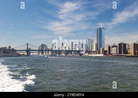 Ein atemberaubender Blick auf die Skyline von NYC von einer Fähre, die nach Uptown fährt, mit hoch aufragenden Gebäuden, der Manhattan Bridge und sanften Wellen im Wasser Stockfoto