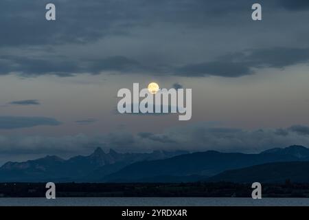 Der fast Vollmond hinter den Alpen an einem bewölkten Tag Stockfoto