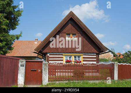 Braunes Holzhaus mit einem Giebeldach und roten Rollläden, umgeben von einem Holzzaun und Blumen, altes Holzhaus, Vesec u Sobotky, Dorfschutz Ar Stockfoto