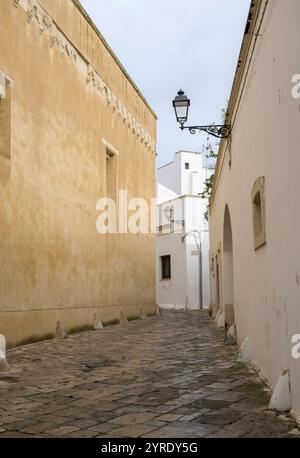 Enge, gepflasterte Gasse zwischen sandfarbenen und weißen Gebäuden mit nostalgischer Straßenbeleuchtung, Altstadt von Galatina, Apulien, Süditalien, Ita Stockfoto