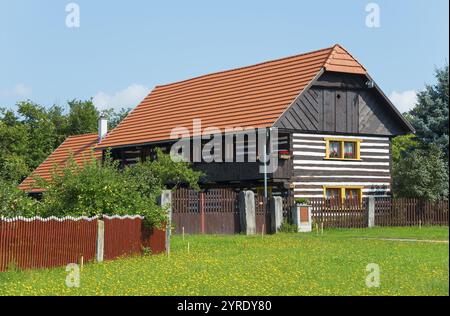 Ein traditionelles Holzhaus mit einem roten Dach, umgeben von einem Holzzaun und einer Wiese mit gelben Blumen, altes Holzhaus, Vesec u Sobotky, Dorf Stockfoto