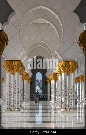 Reich verzierter Innenkorridor der Scheich-Zayed-Moschee mit goldenen, palmenförmigen Kapitellen und Marmorblumensäulen in Abu Dhabi, VAE. Stockfoto