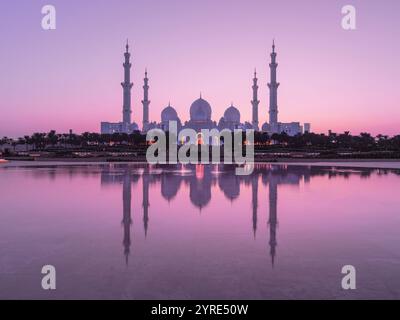 Die große Moschee von Scheich Zayed leuchtet in den sanften rosafarbenen Tönen der Dämmerung, reflektiert auf dem ruhigen Wasser und zeigt berühmte Kuppeln und Minarette in Abu Dhabi Stockfoto