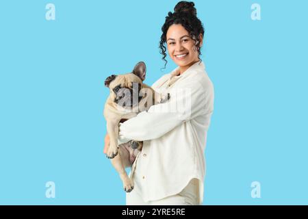 Glückliche junge afroamerikanische Frau mit süßer französischer Bulldogge auf blauem Hintergrund Stockfoto