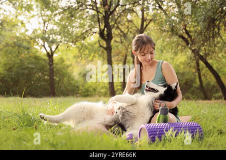 Sportliche junge Frau mit süßem Husky-Hund, der auf Yogamatte im Park sitzt Stockfoto