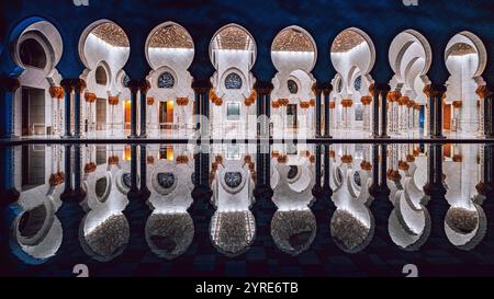 Beleuchtete Kolonnade der Scheich-Zayed-Moschee mit atemberaubenden Reflexionen im Innenhof Pool bei Nacht, Abu Dhabi, VAE. Stockfoto