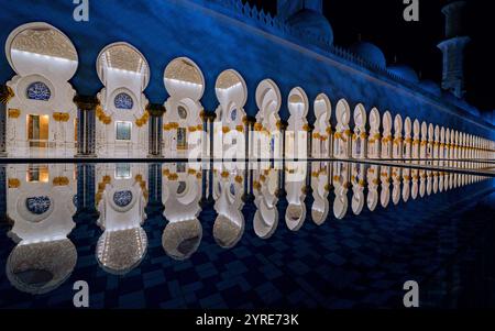 Beleuchtete Kolonnade der Scheich-Zayed-Moschee mit atemberaubenden Reflexionen im Innenhof Pool bei Nacht, Abu Dhabi, VAE. Stockfoto