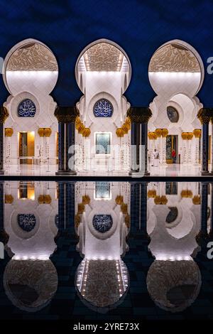 Beleuchtete Kolonnade der Scheich-Zayed-Moschee mit atemberaubenden Reflexionen im Innenhof Pool bei Nacht, Abu Dhabi, VAE. Stockfoto