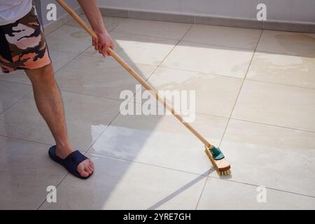 Mann, der die Fliesen am Pool mit einer Bodenscheuerbürste reinigt Stockfoto