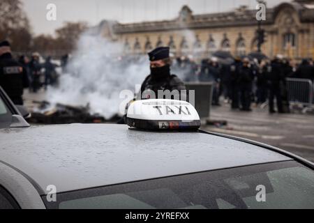 Paris, Frankreich. Dezember 2024. Während der Demonstration der französischen Taxifahrer steht ein Polizeibeamter in der Nähe eines Taxis. Am zweiten Tag der Demonstrationen von Taxifahrern in Frankreich blockierten Dutzende von Fahrzeugen die Straßen in der Nähe der Nationalversammlung, um an der Esplanade des Invalides in Paris zu protestieren. Die Arbeiter fordern die Aufgabe der Maßnahmen, die den Taxi-Transport für die Patienten bedrohen, bekämpfen den illegalen Wettbewerb, fördern Taxis als einen wesentlichen öffentlichen Dienst. Quelle: SOPA Images Limited/Alamy Live News Stockfoto