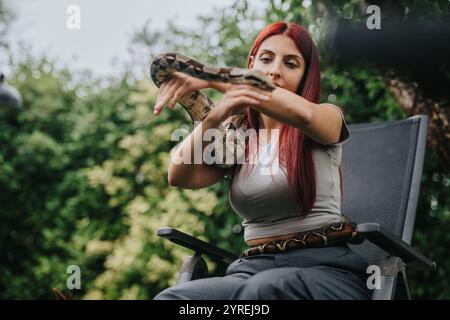 Mädchen, das draußen sitzt und eine große Schlange mit Neugier hält Stockfoto
