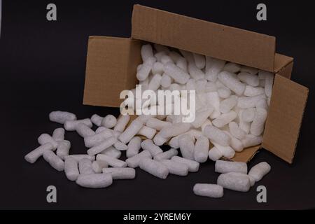 Offene Pappschachtel mit weißem Polystyrolschaum, die Erdnüsse auf dunklem Hintergrund verpackt, symbolisiert leichte und sichere Verpackungen für zerbrechliche Gegenstände Stockfoto