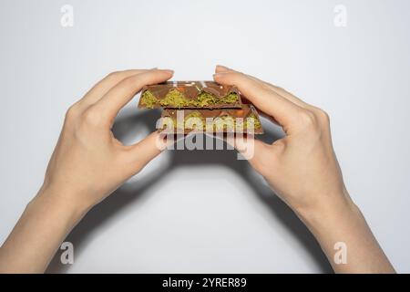 Trend Dubai Schokoladenriegel mit Pistazienpaste, Tahini und Kataifi-Teig in den Händen der Frau. Süßwaren und Süßwaren. Stockfoto