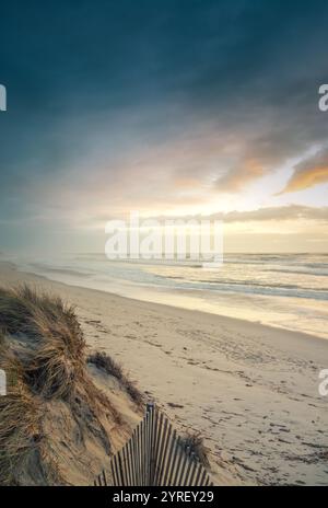 Warmer Sonnenaufgang, der Sandstrand und die Meereswellen mit einem Holzzaun zum Strand Rodanho, viana do castelo, portugal, beleuchtet Stockfoto