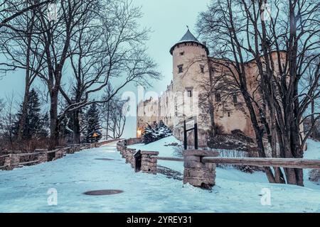 Schneebedeckter Pfad zur majestätischen Burg Niedzica, die von sanftem Dämmerungslicht beleuchtet wird und eine ruhige Winterszene in der polnischen Landschaft schafft Stockfoto