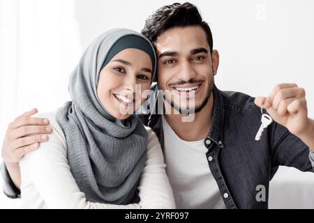Glückliche muslimische Familie, die sich auf Papierkartons stützt und Schlüssel zeigt Stockfoto