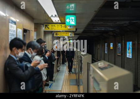 Menschen, die an einem Bahnhof in Tokio auf einen Zug warten, mit einer lebhaften, modernen urbanen Atmosphäre, die das tägliche Leben in der Stadt widerspiegelt. Stockfoto