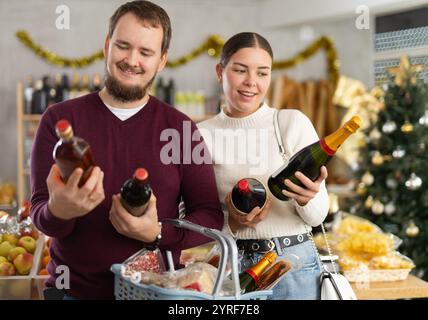 Glückliches verheiratetes Paar, das Alkohol im Lebensmittelbereich des Supermarktes wählt, um Weihnachten zu feiern Stockfoto