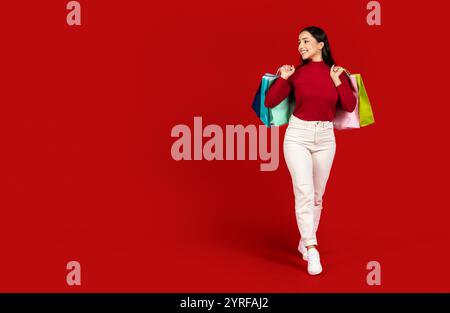 Junge Frau, die fröhlich mit bunten Taschen in einer lebhaften Umgebung einkaufen geht Stockfoto